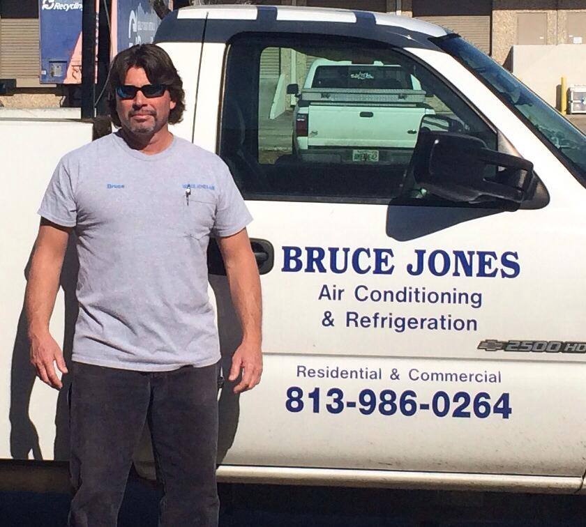 HVAC technician standing by Bruce Jones Air Conditioning & Refrigeration service truck outside a commercial building